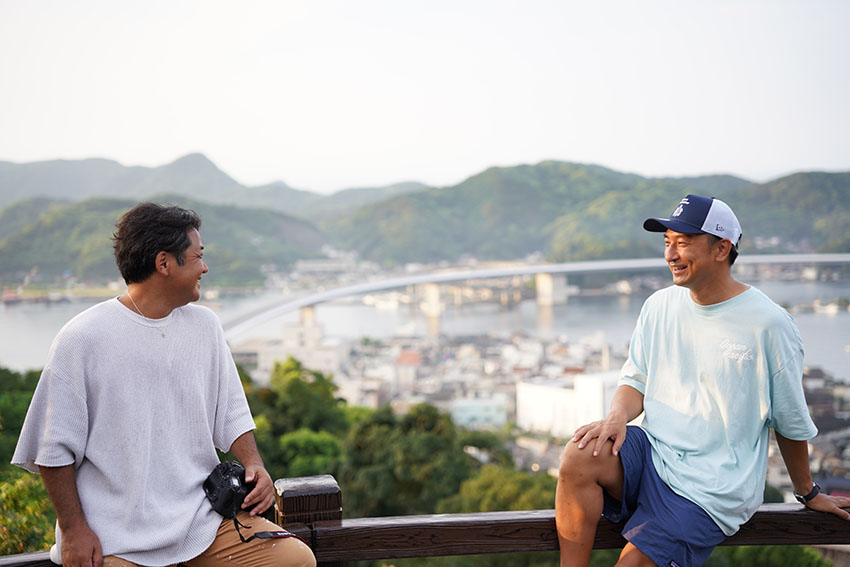 ハイヤ大橋をバックに映る鍵井さんと河本